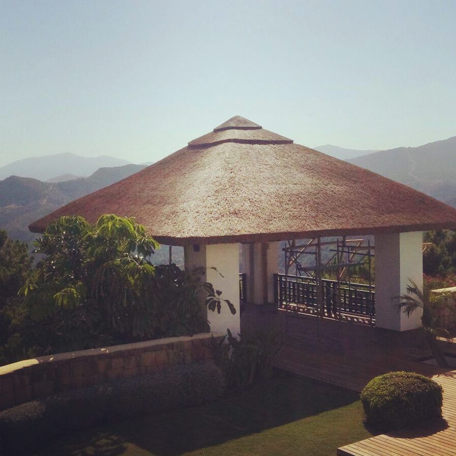 Cenador con techo de paja con vistas a las montañas y la vegetación en un día soleado.