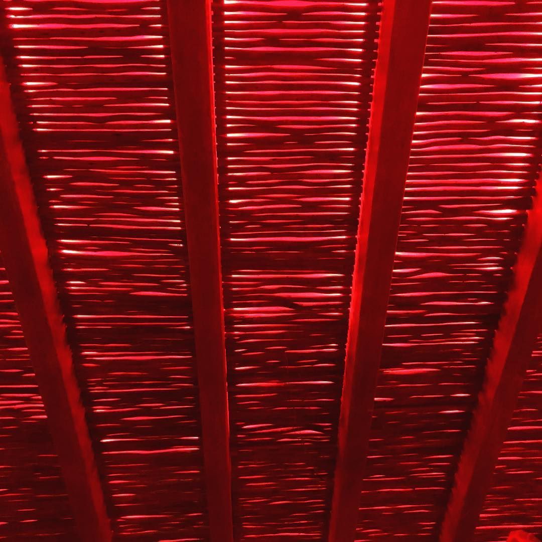 Vista en tonos rojizos de un techo de listones, probablemente una pérgola o toldo, con vigas de madera.