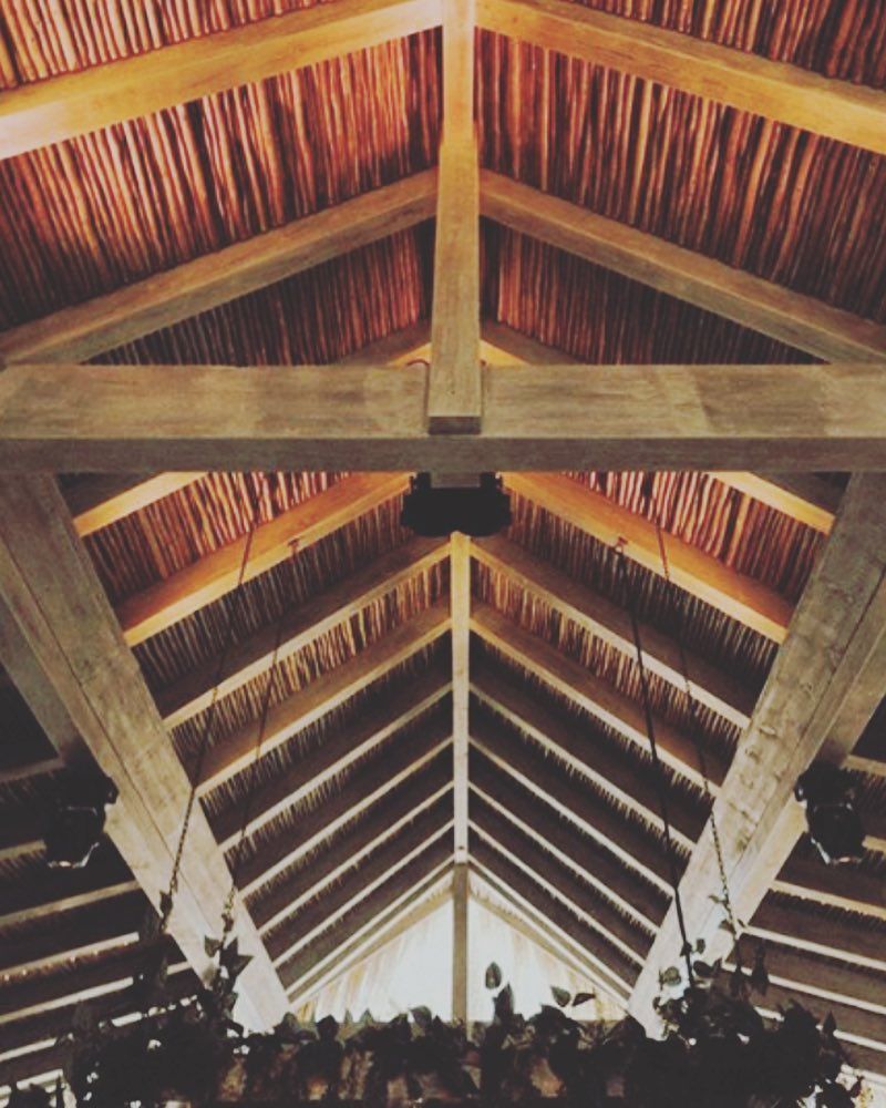 Techo de madera con vigas y cara inferior texturizada de color rojizo, posiblemente de paja.