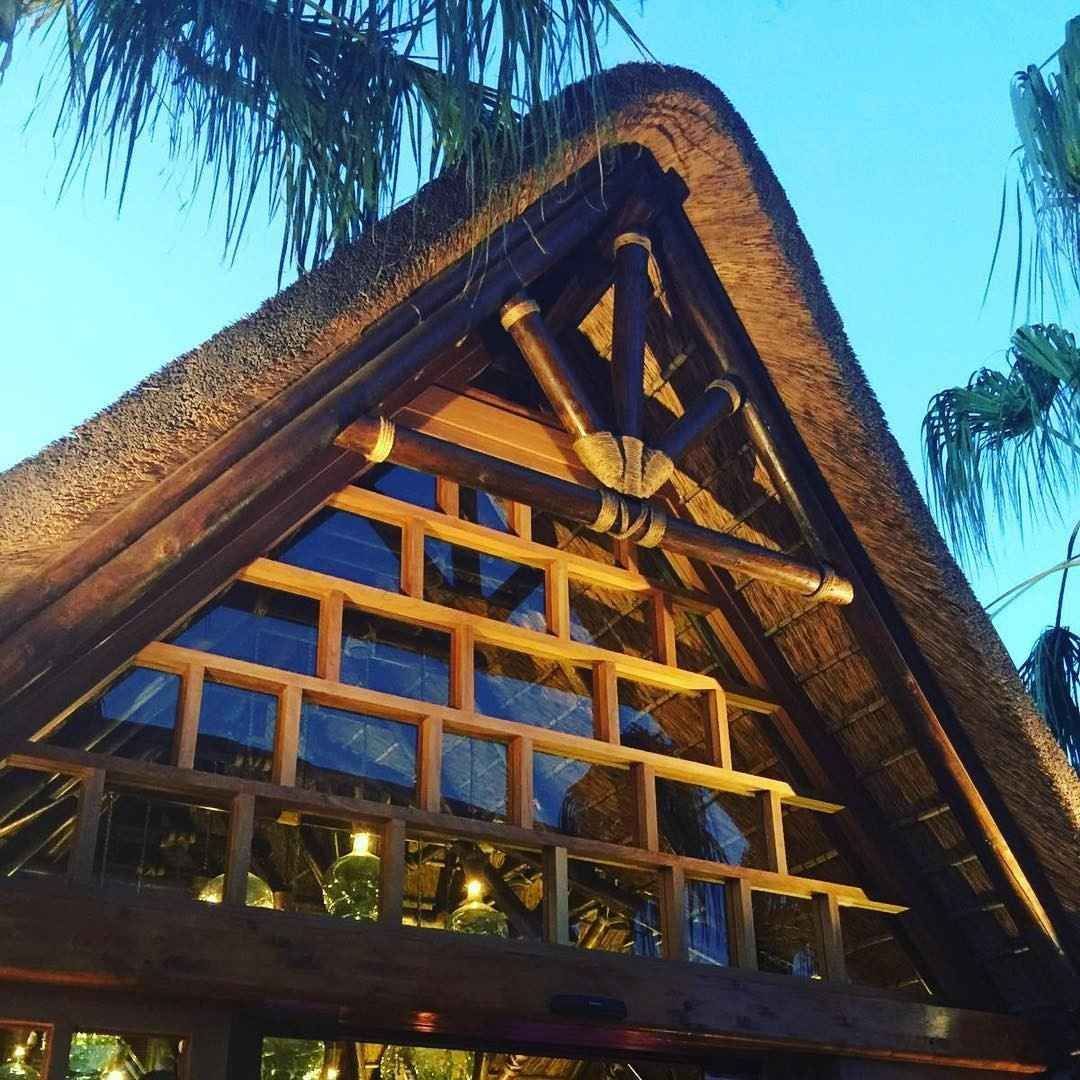 Estructura de techo de paja con vigas de madera y una ventana triangular.