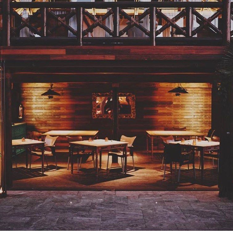 Interior de restaurante vacío con paredes de madera, mesas y sillas. Iluminación cálida.