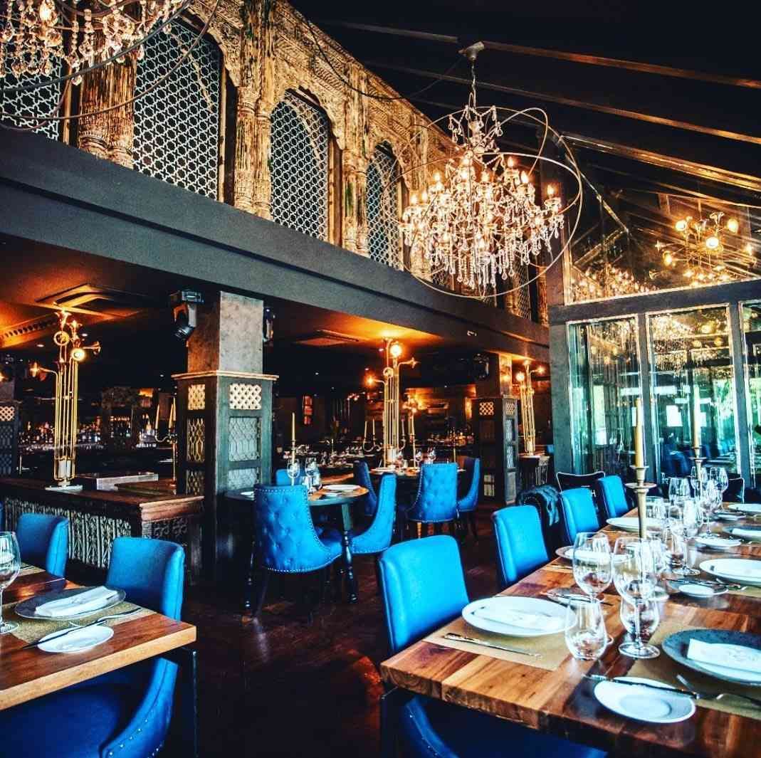 Interior de restaurante con sillas azules, mesas de madera y candelabros ornamentados.