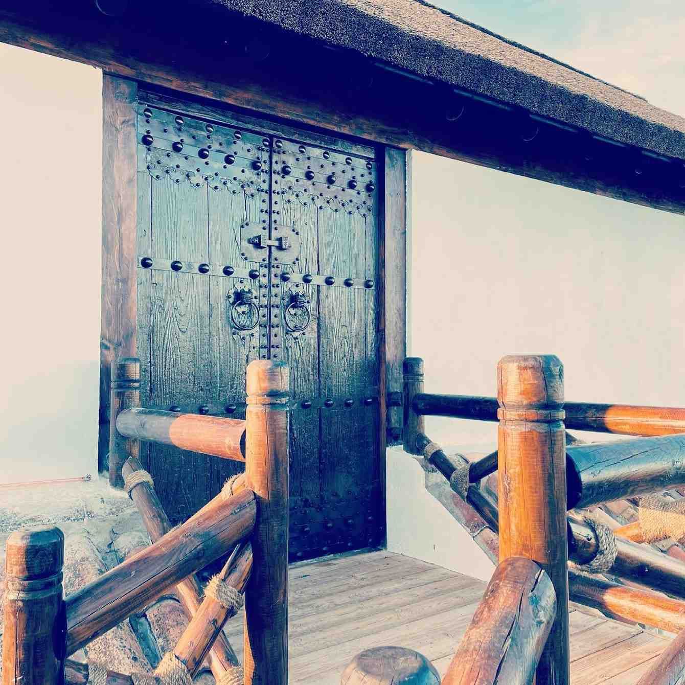 Puerta de madera con tallas detalladas, a la que se accede a través de un puente de madera.