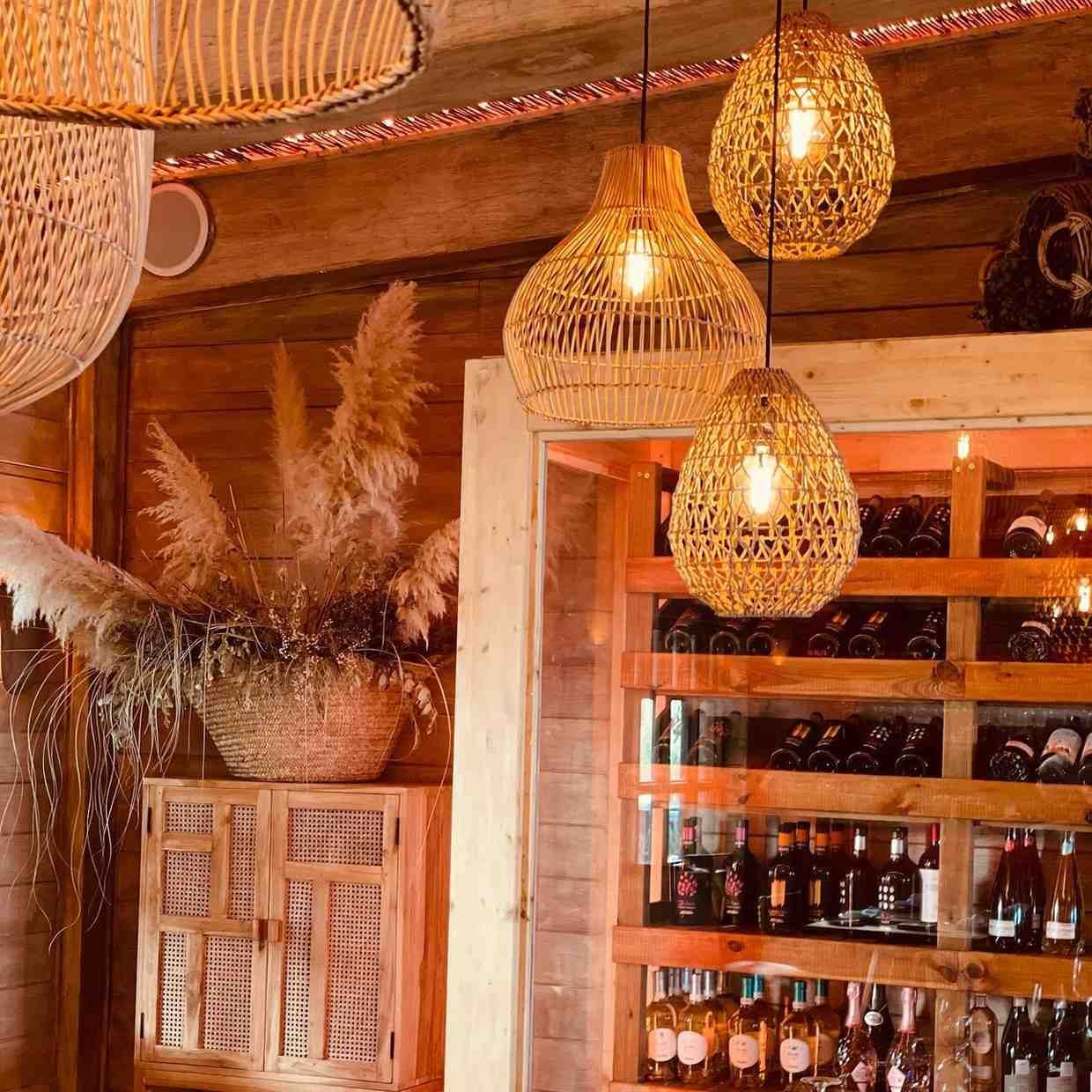Las luces colgantes tejidas iluminan una barra rústica con un botellero de madera y plantas secas decorativas.