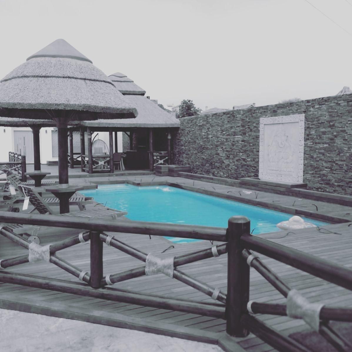 Piscina con cabañas con techo de paja y terraza de madera.