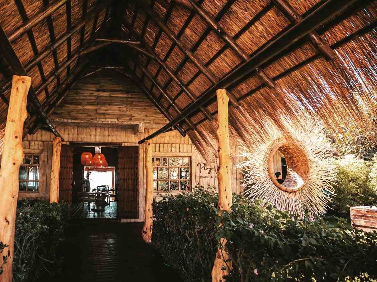 Exterior de edificio rústico con techo de paja, vigas de madera y una corona decorativa natural.