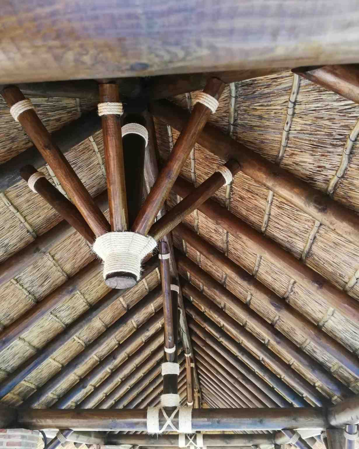 Estructura de techo de paja de madera con vigas que irradian desde un punto central, adornado con detalles de cuerdas.