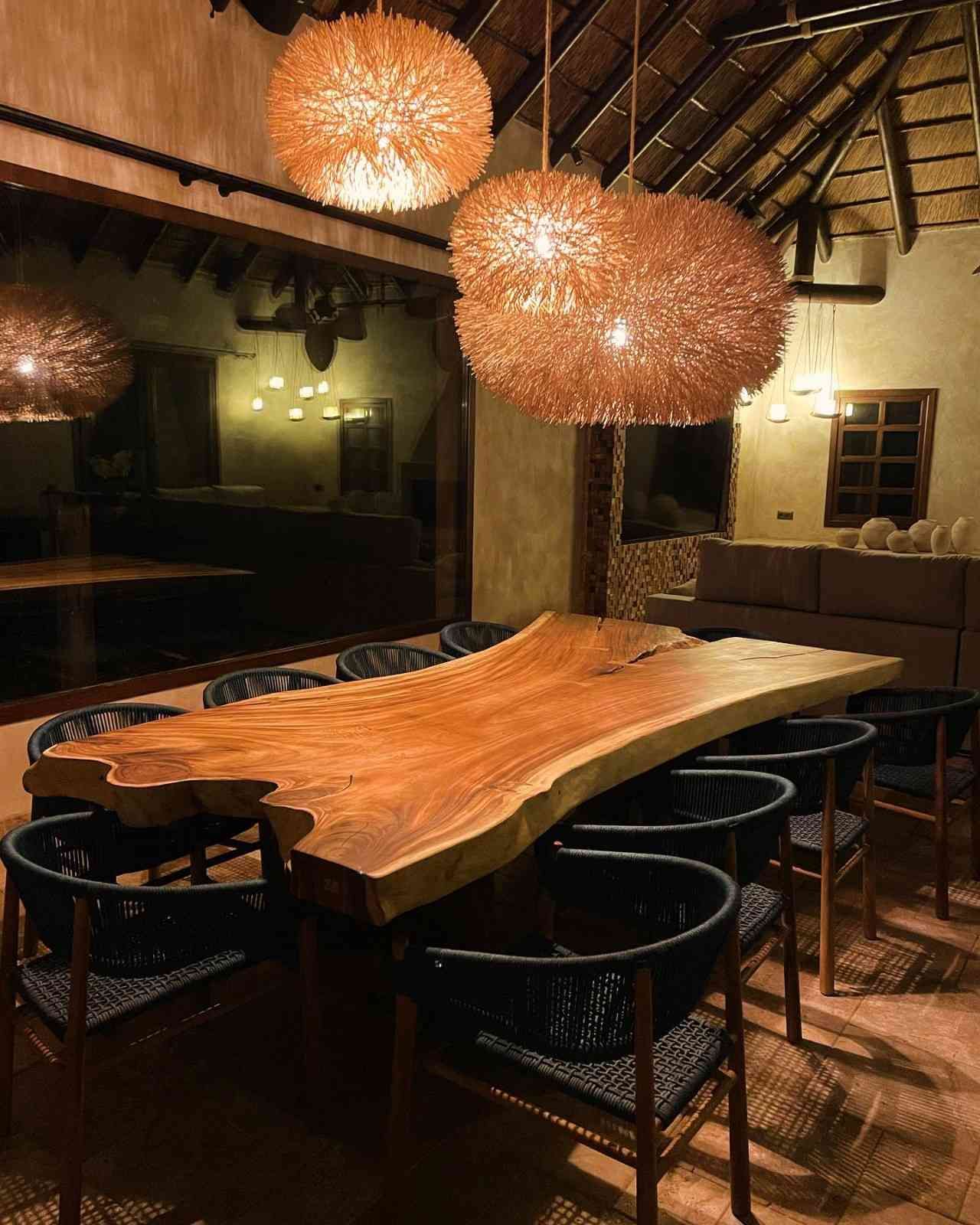 Gran mesa de comedor de madera con sillas, bajo luces decorativas en forma de globo.