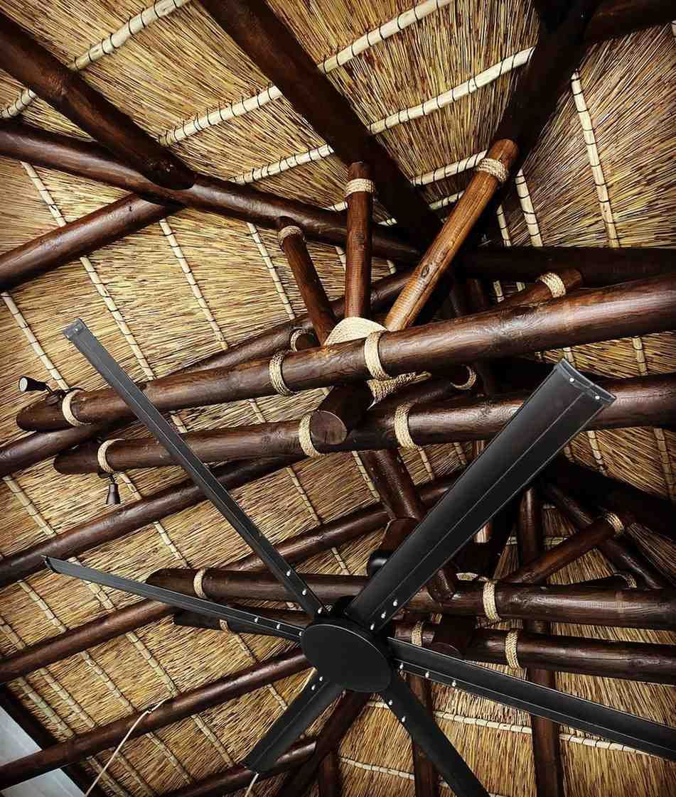 Techo oscuro con vigas de madera, techo de paja y gran ventilador de techo negro.