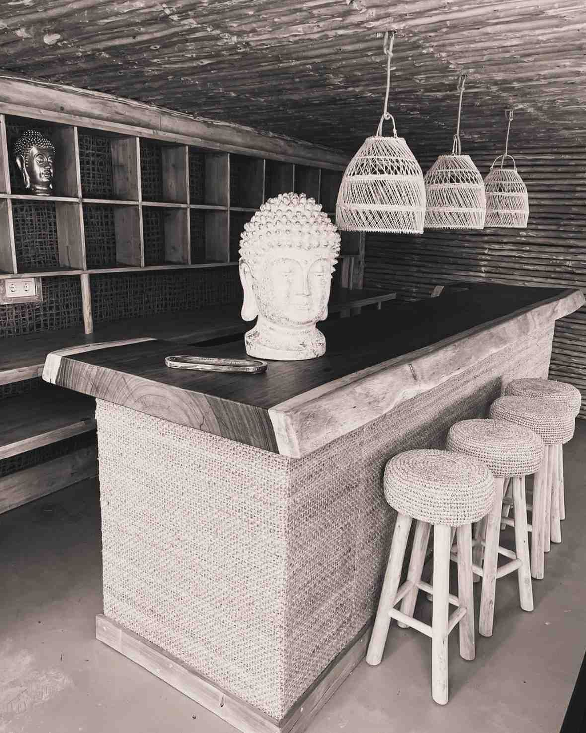 Bar con detalles tejidos y estatua de cabeza de Buda, con lámparas colgantes y taburetes.