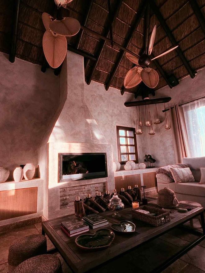 Acogedora sala de estar con chimenea, techo de paja y ventiladores de techo. Un sofá, una mesa de centro.