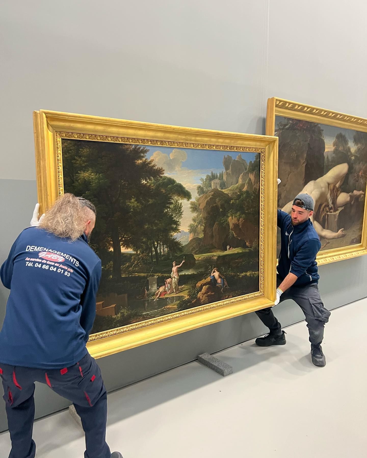 Deux déménageurs qui soulèvent un tableau dans un musée