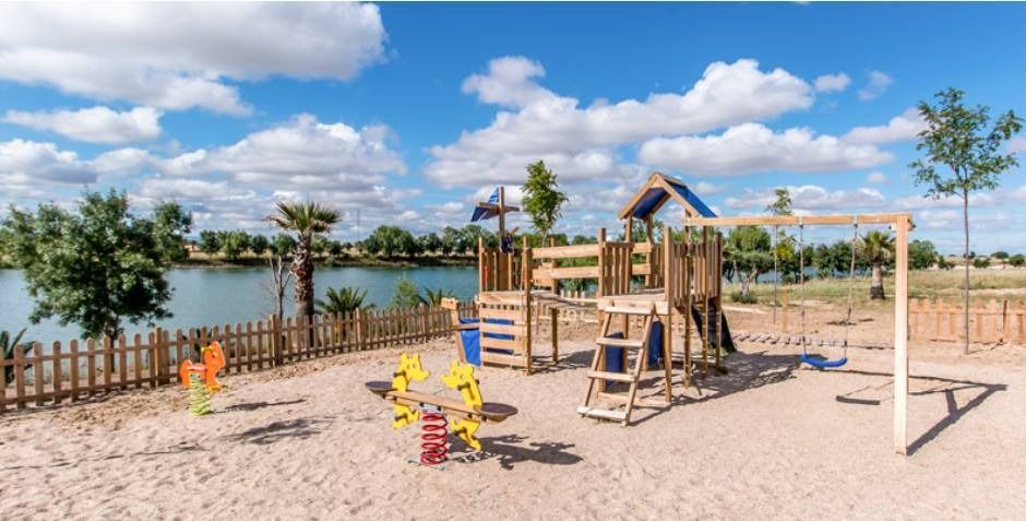 Un parque infantil con una valla y un lago al fondo.