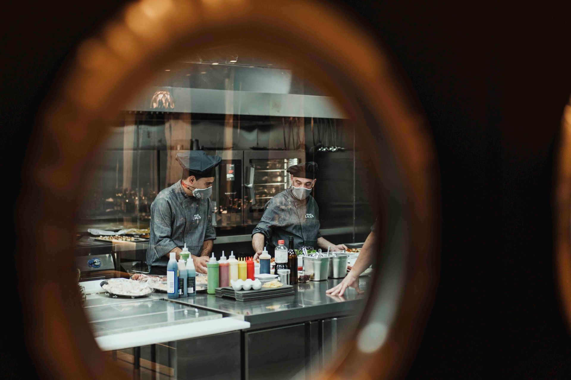 Dos chefs con máscaras están preparando comida en una cocina.
