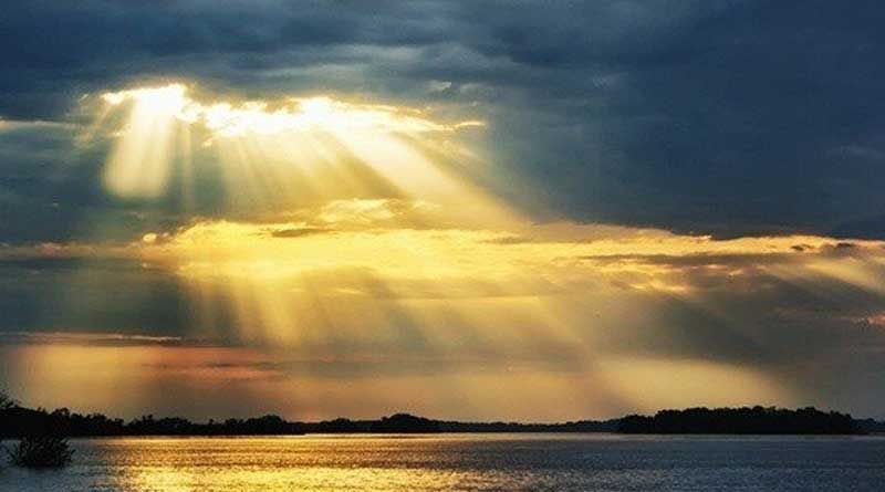 El sol brilla a través de las nubes sobre un cuerpo de agua.