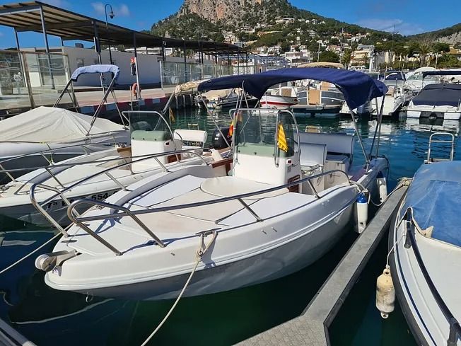 Un barco blanco con un toldo azul está atracado en un puerto deportivo.