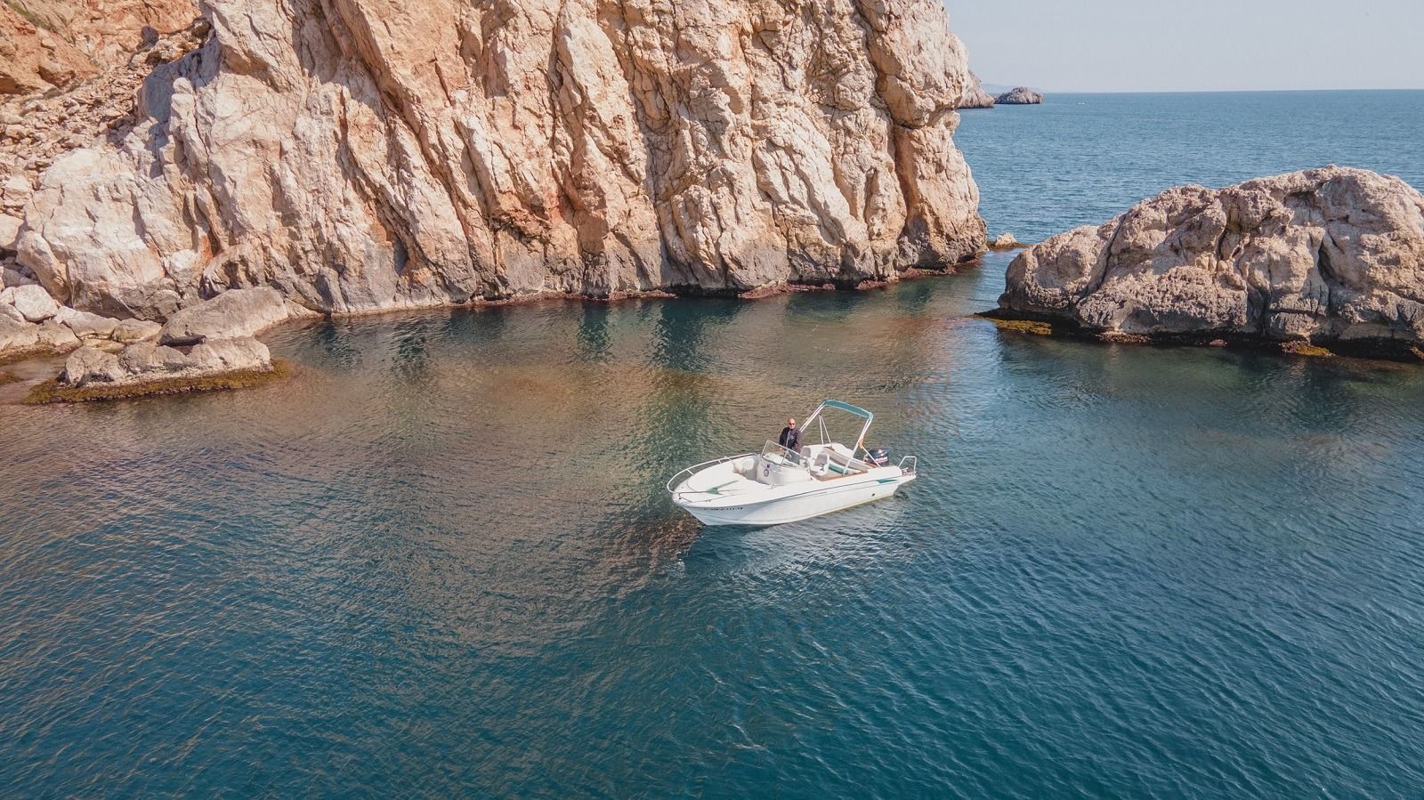 Un barco flota en el océano cerca de un acantilado rocoso.