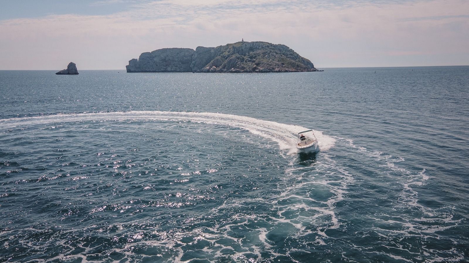 Un barco navega por el océano con una pequeña isla al fondo.