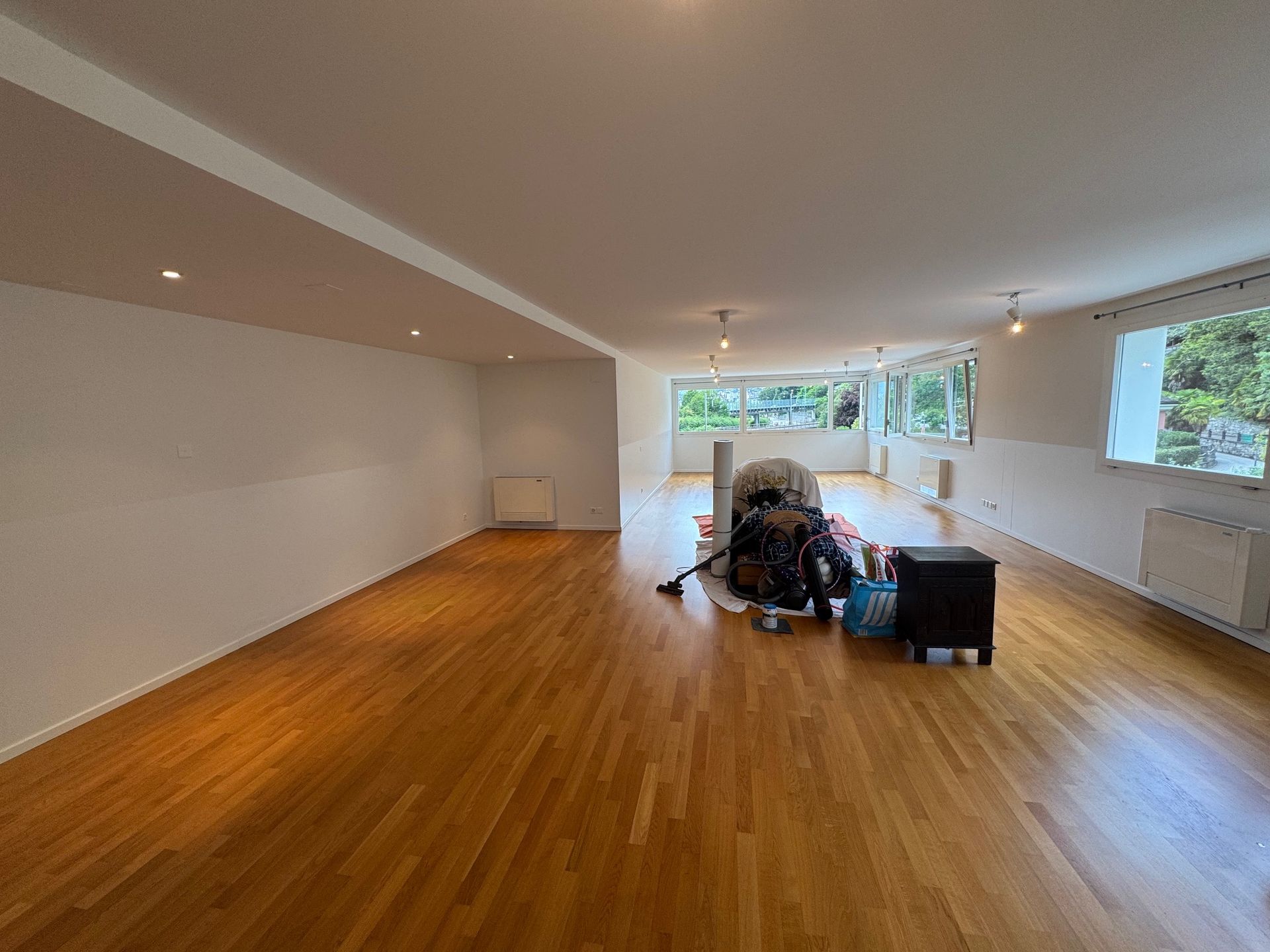 Grande specchio con cornice nera su parete beige testurizzata che riflette uno spazio di archiviazione, porta sulla destra.