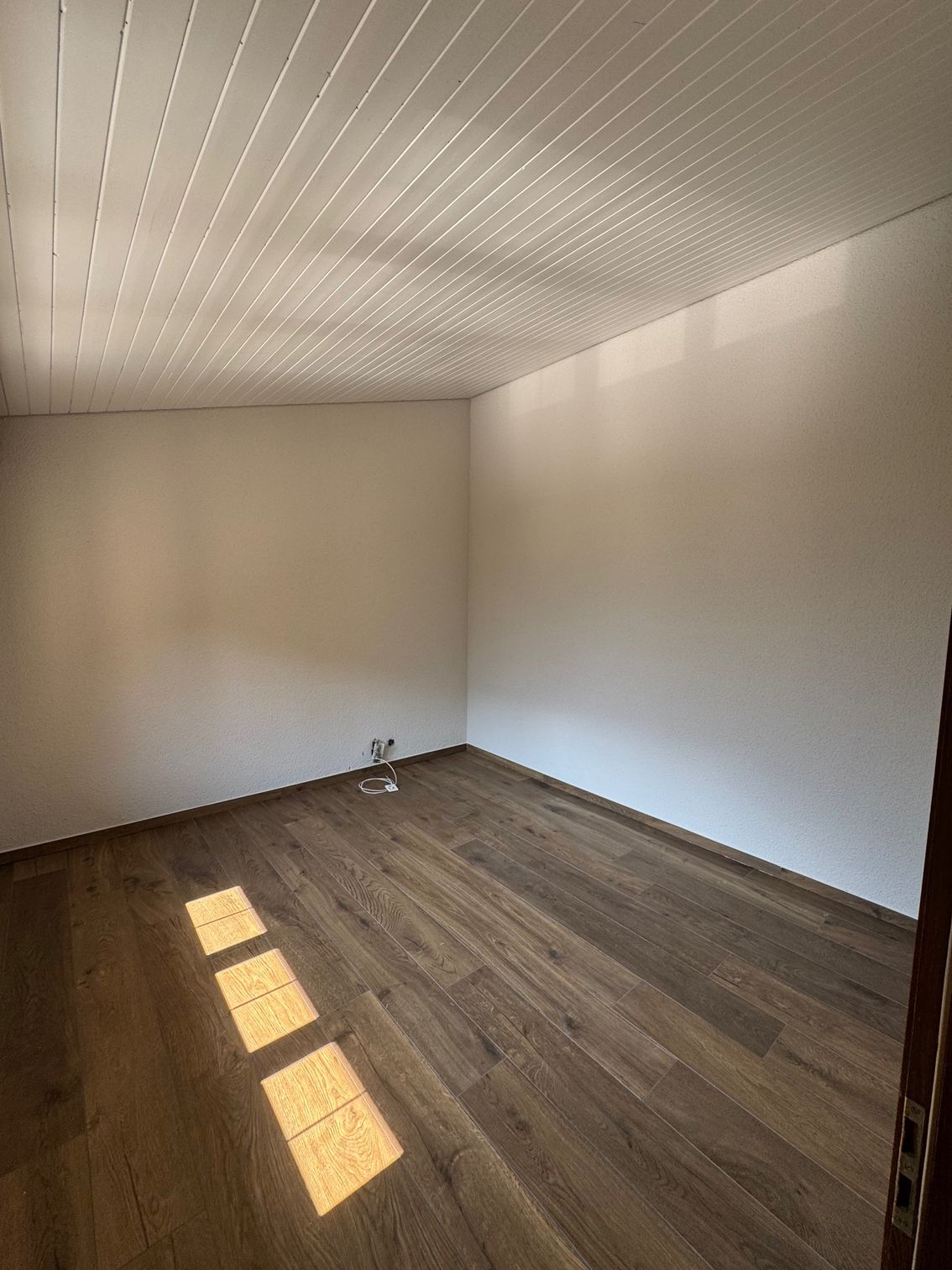 Casa grigia con finestre con cornice bianca, tetto scuro, grondaia in rame e scale esterne.