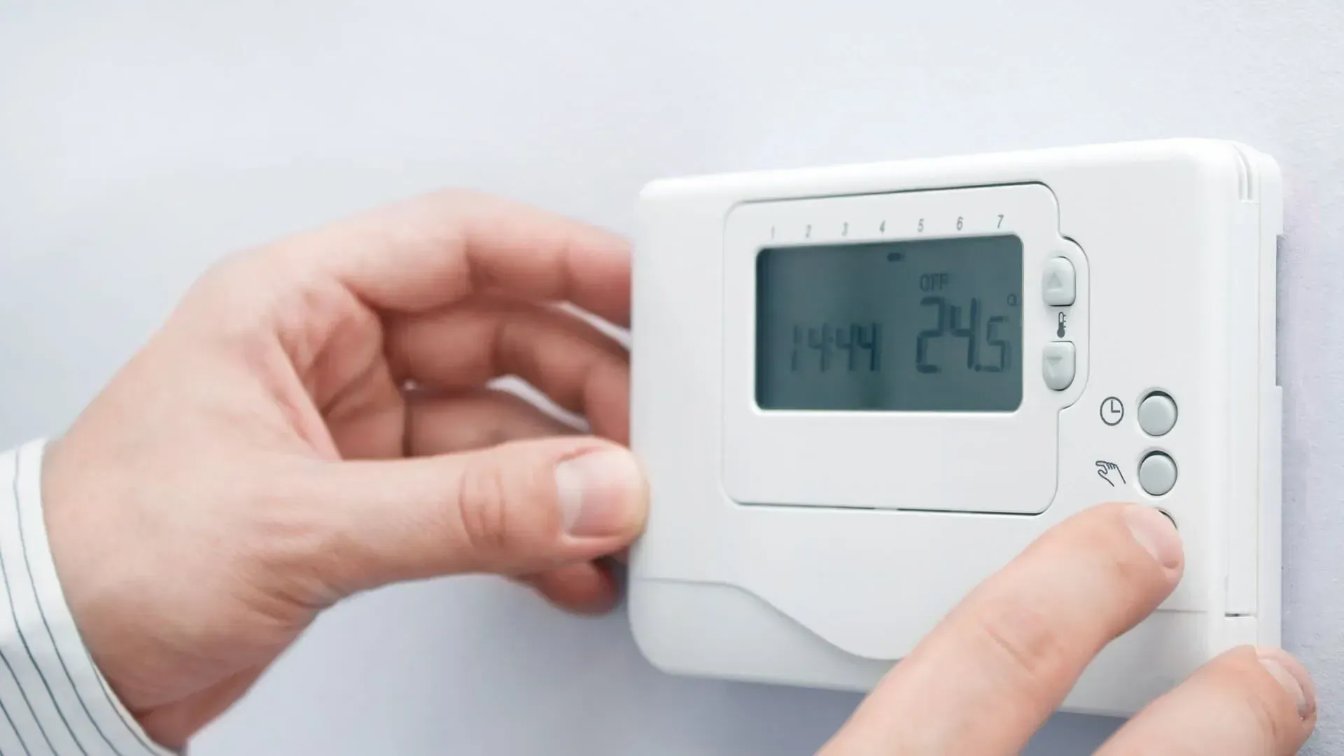 Pessoa ajustando um termostato branco em uma parede branca, definindo a temperatura para 24,5 graus.