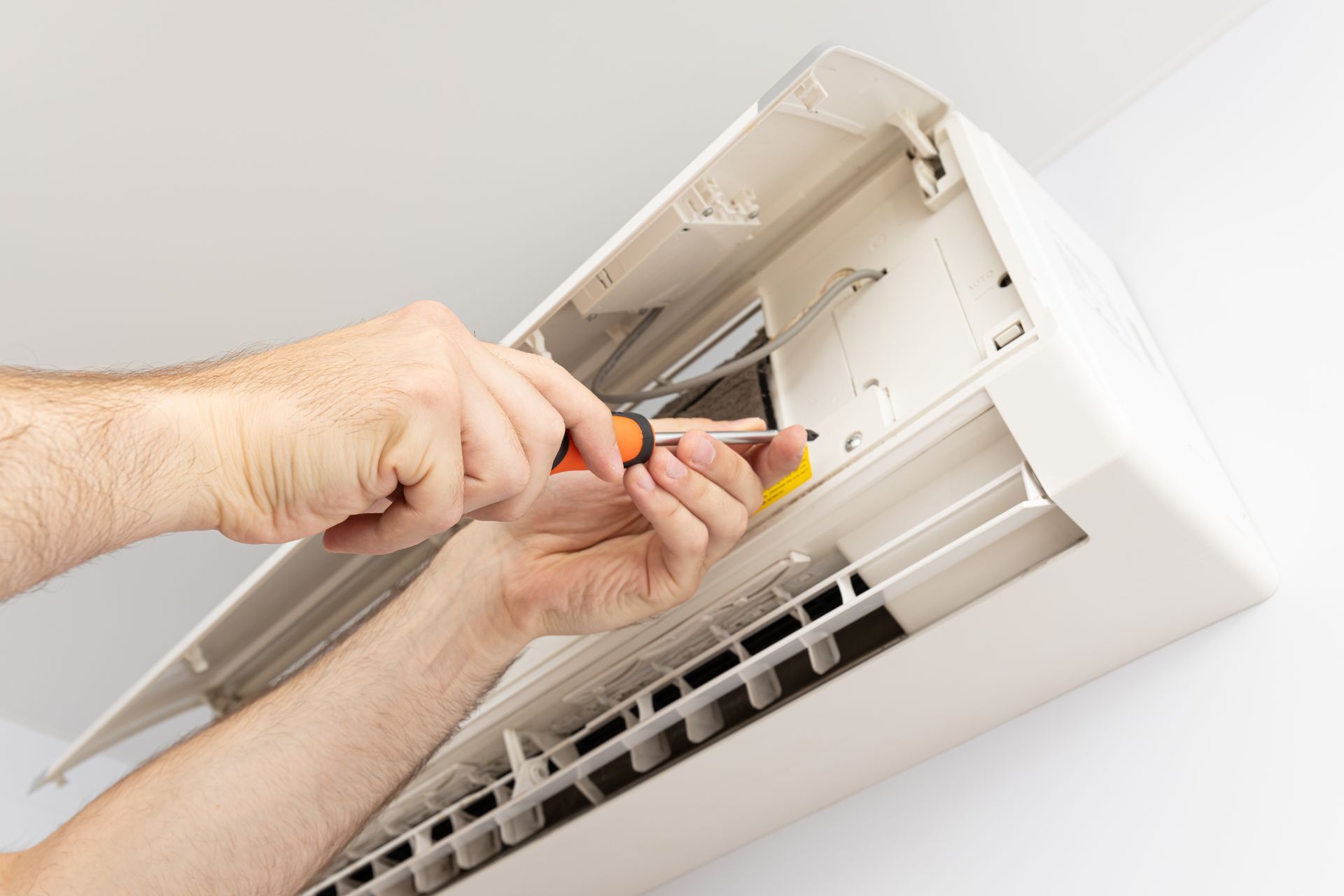 Pessoa de camisa branca e chapéu trabalhando em uma unidade de ar condicionado, curvada e manuseando um cano do lado de fora.