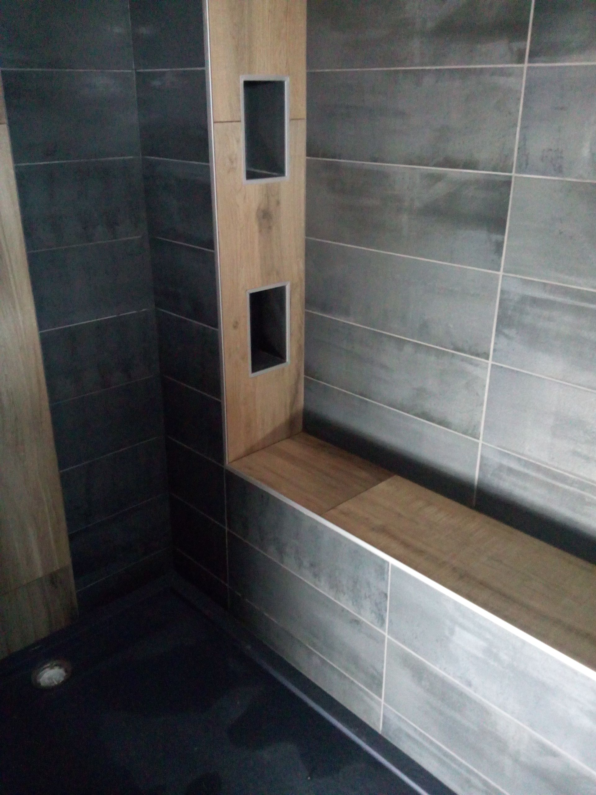 Une cabine de douche moderne avec des carreaux muraux rectangulaires gris, un banc carrelé imitation bois et deux niches murales intégrées.