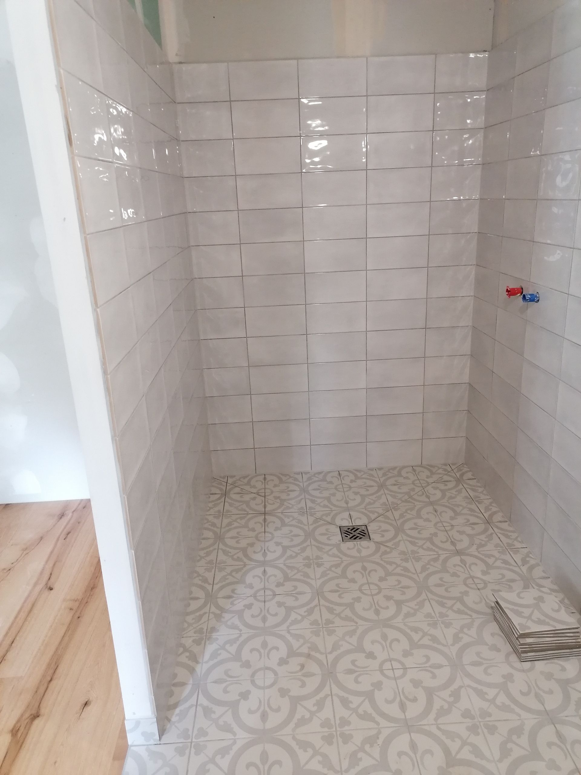 Une douche en construction avec des carreaux de métro blancs aux murs et des carreaux décoratifs gris et blancs à motifs au sol.