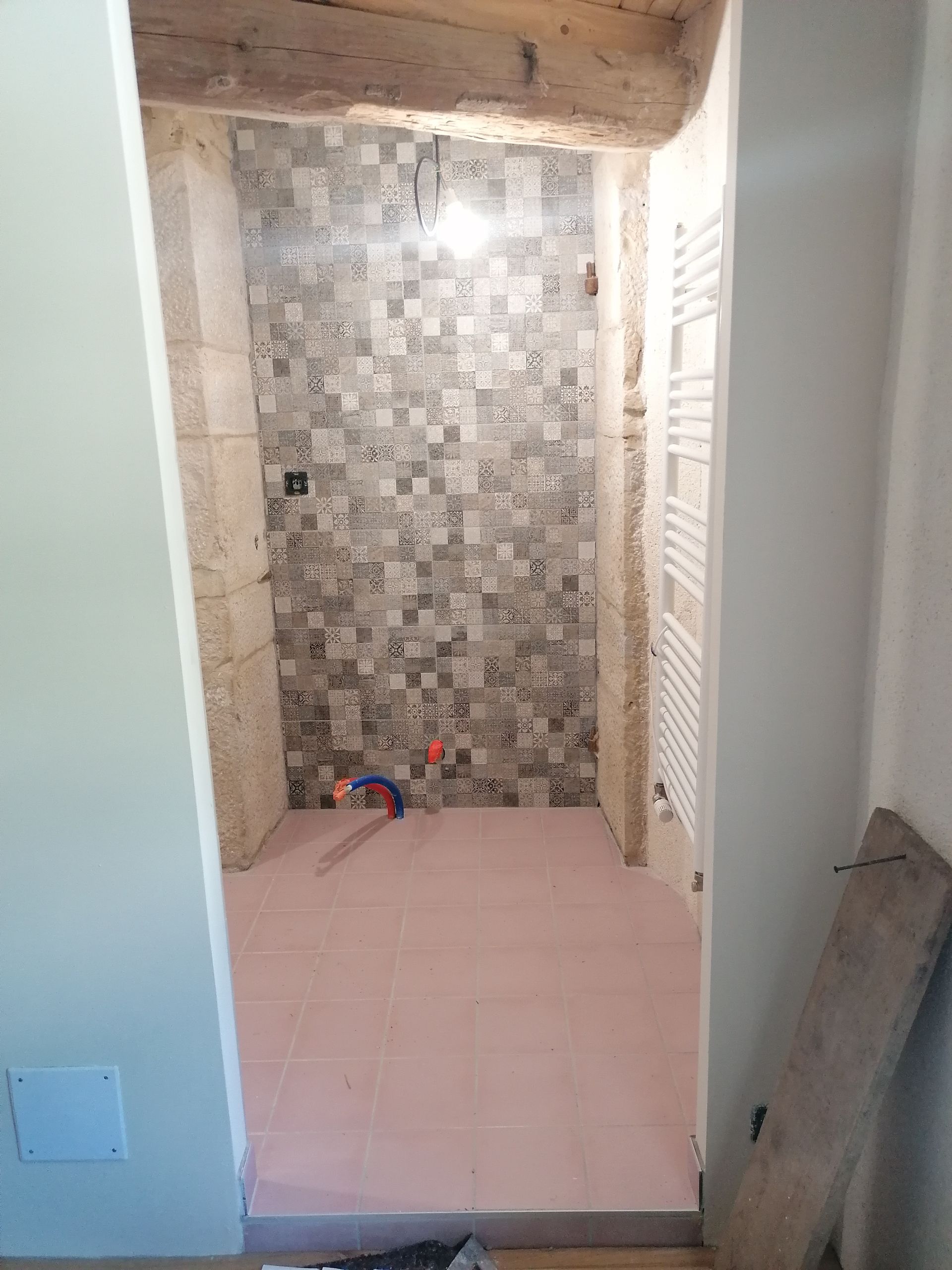Rénovation de la salle de bains en cours, avec crédence carrelée, plomberie et sous-couche rose au sol.
