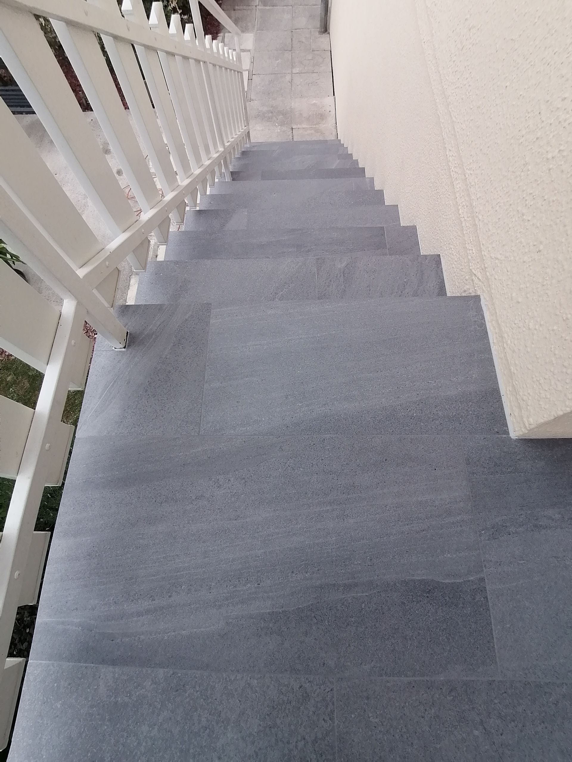 Vue plongeante d'un escalier en béton gris avec une rampe blanche à gauche et un mur beige à droite.