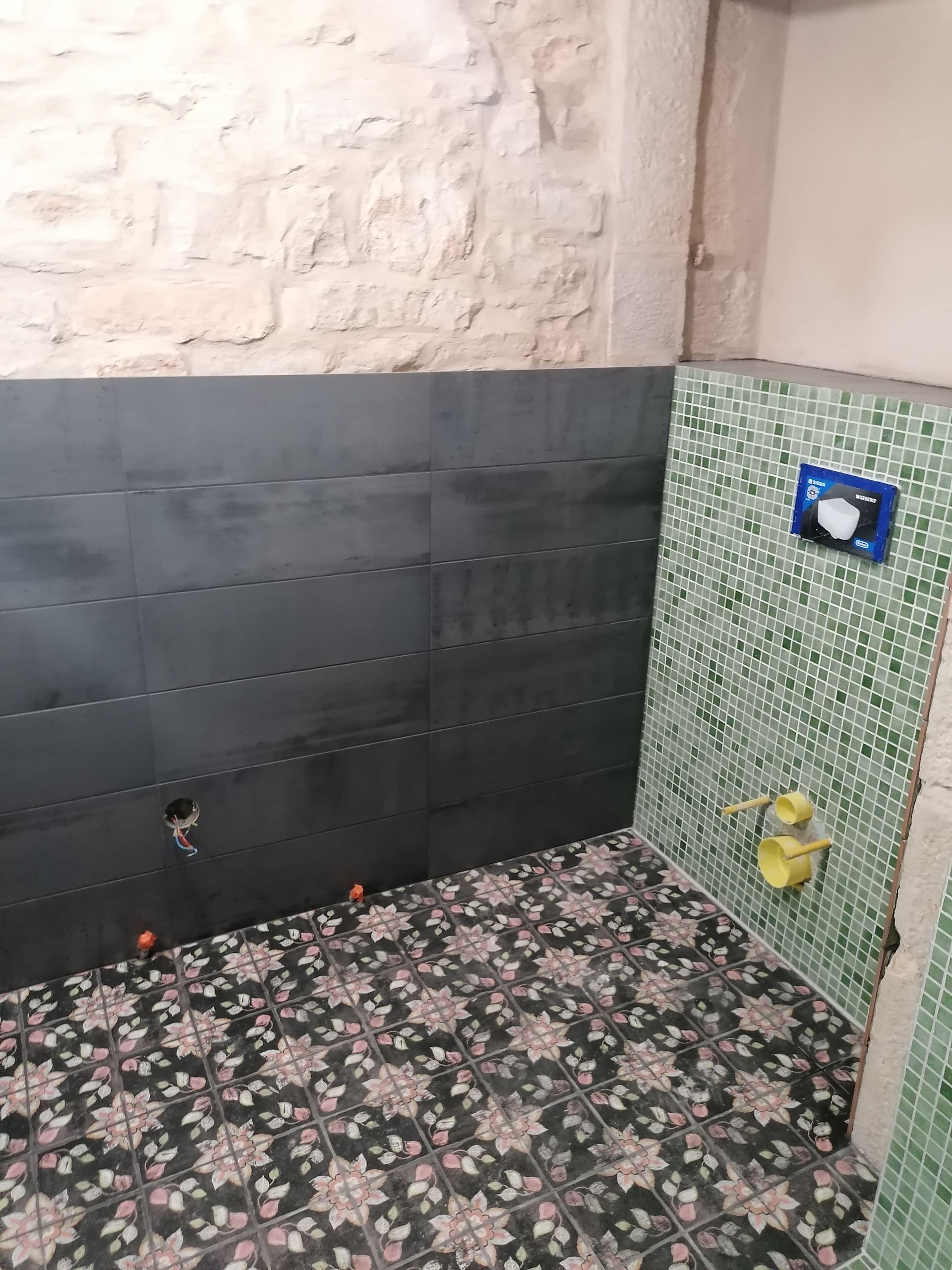 Intérieur de salle de bains avec carrelage horizontal gris foncé, accents de mosaïque verte aux murs et carrelage à motifs au sol.