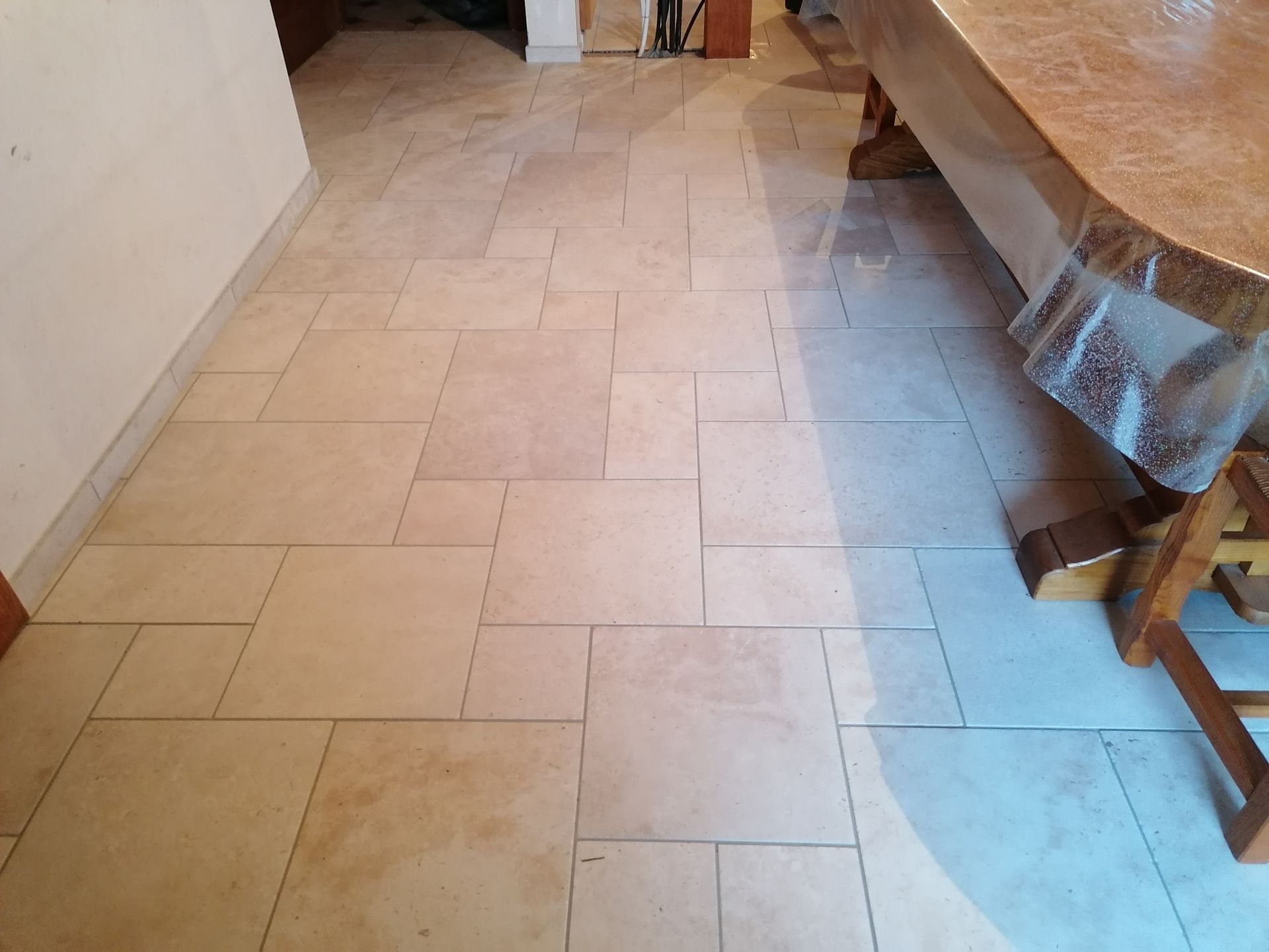 Un sol carrelé en pierre à motif rectangulaire décalé, partiellement éclairé par la lumière naturelle près d'une table en bois.