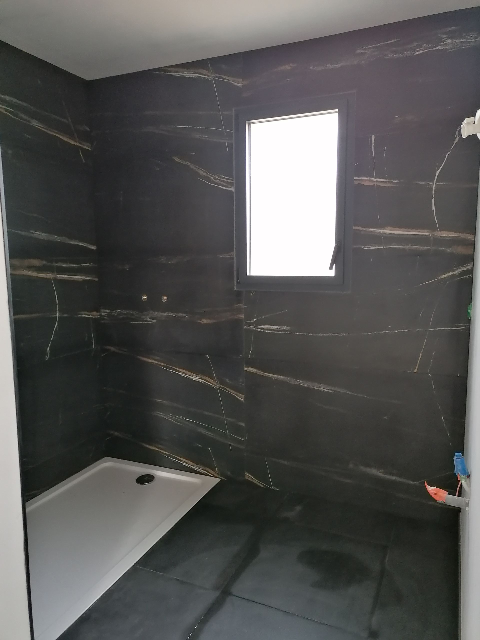 Salle de bains en rénovation avec carrelage mural foncé veiné, receveur de douche blanc et carrelage au sol foncé.