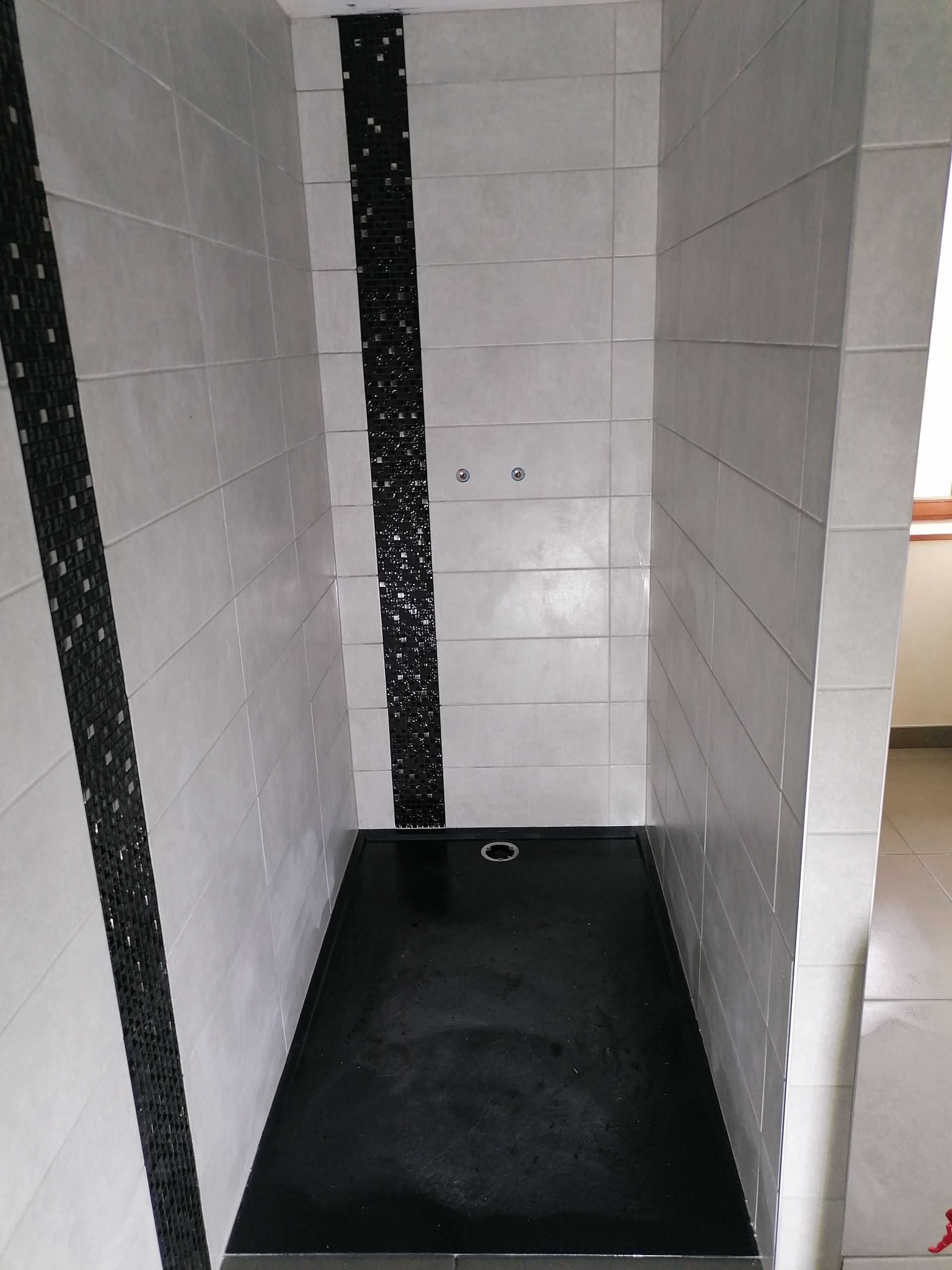 Une cabine de douche carrelée avec des murs gris, deux bandes décoratives noires et un receveur de douche noir.