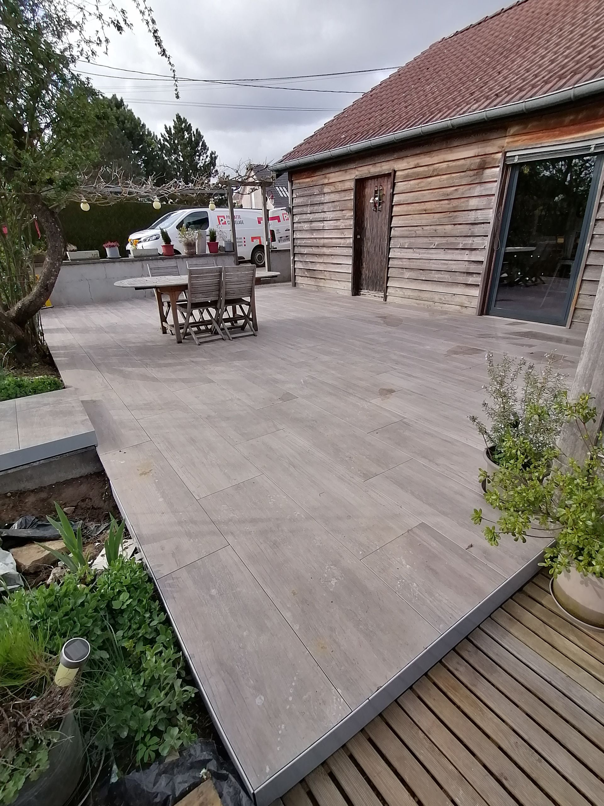 Terrasse en bois avec mobilier de jardin, à côté d'un bâtiment à la façade en bois rustique.