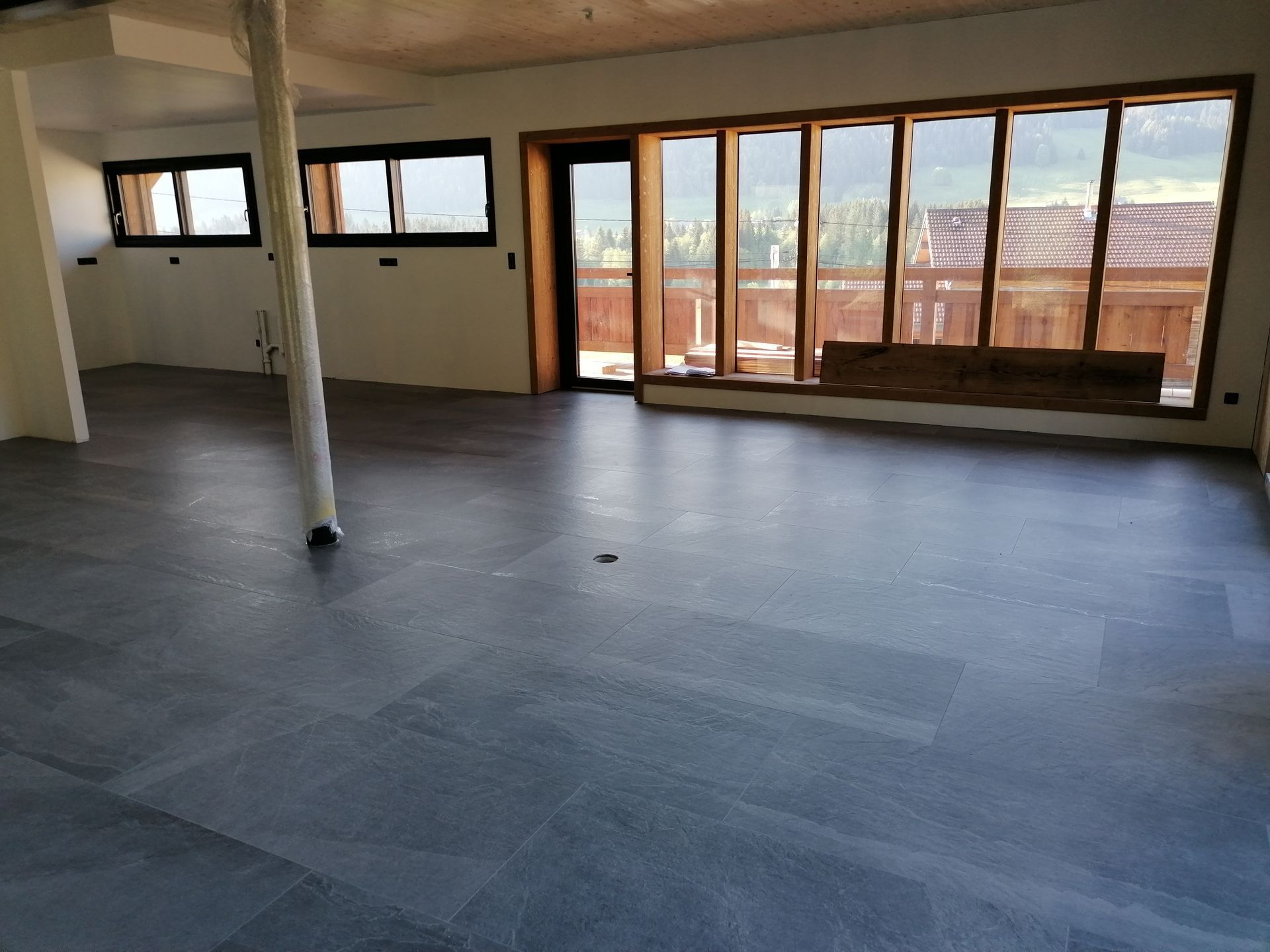 Grande pièce vide avec un sol gris foncé, de grandes fenêtres et une structure en bois.