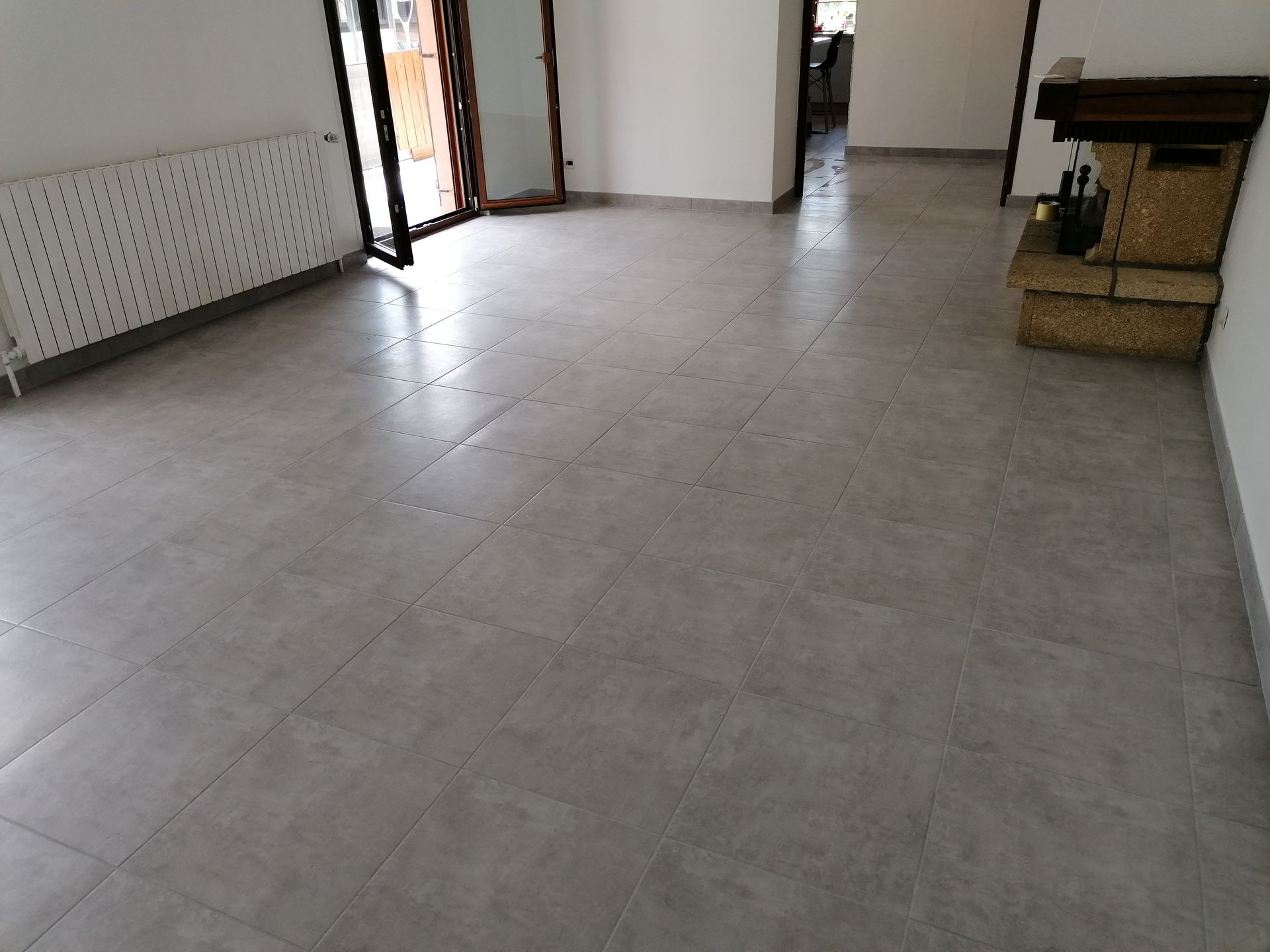 Pièce vide avec un sol carrelé gris, un radiateur blanc sur la gauche et un meuble de rangement tressé dans le coin.