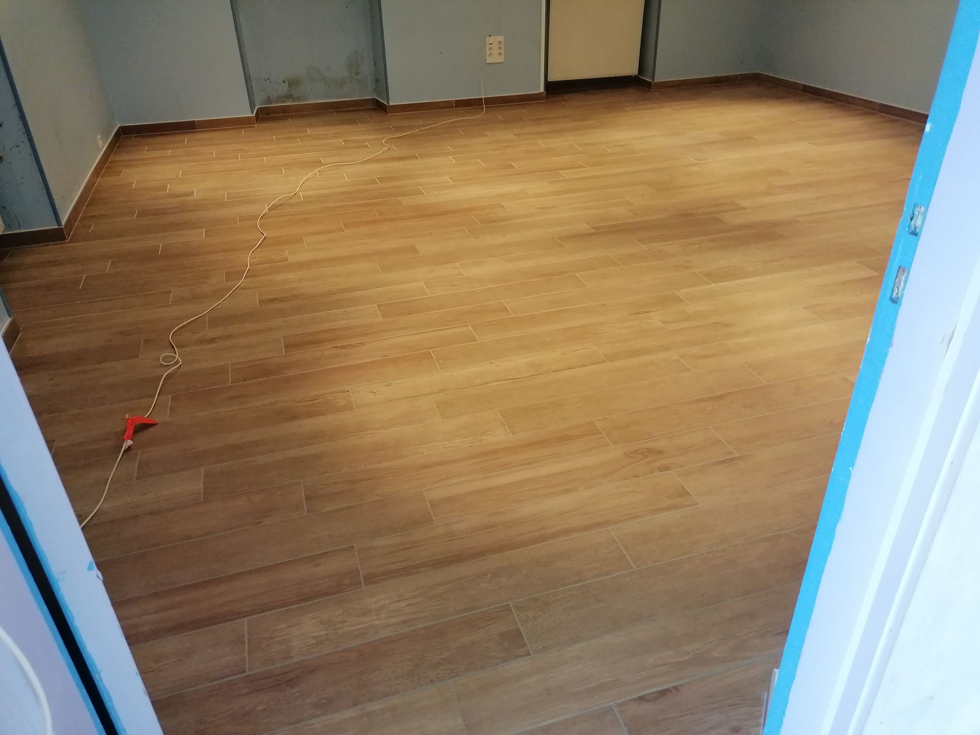 Un sol stratifié imitation bois fraîchement installé dans une pièce vide aux murs bleu clair et une guirlande lumineuse au sol.