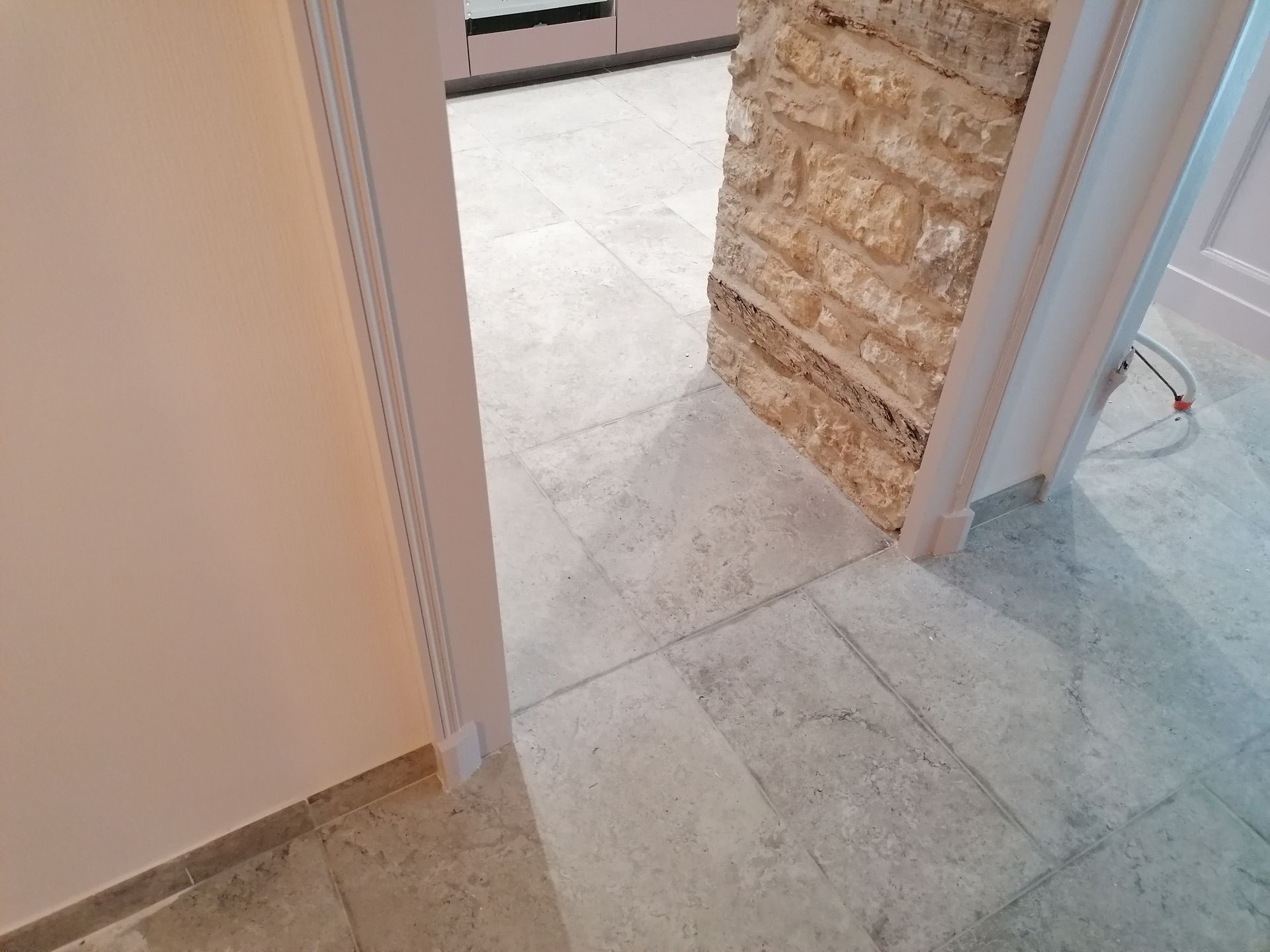 Une porte donnant sur une pièce carrelée, avec un pilier en pierre texturée à côté de carreaux de sol carrés de couleur claire.