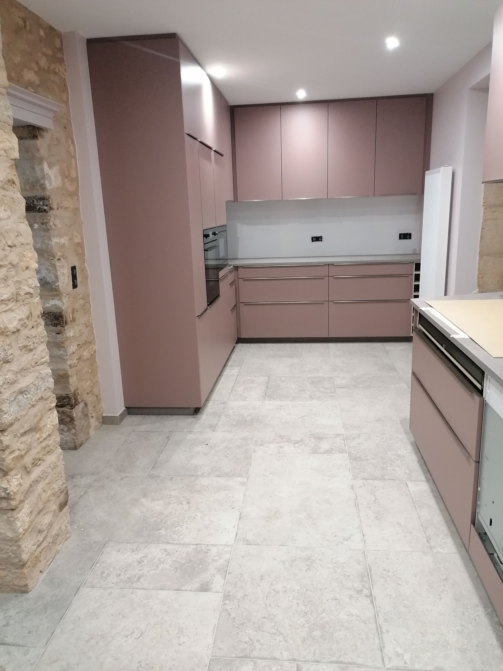 Cuisine en rénovation avec placards mauves, éléments en acier inoxydable et carrelage gris clair.