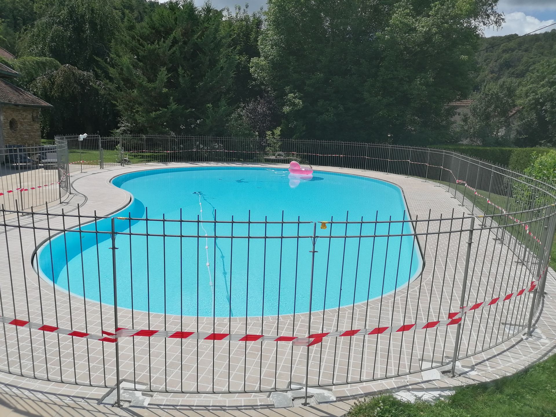 Terrasse en béton avec piscine et chaises longues. Pelouse et arbres en arrière-plan.