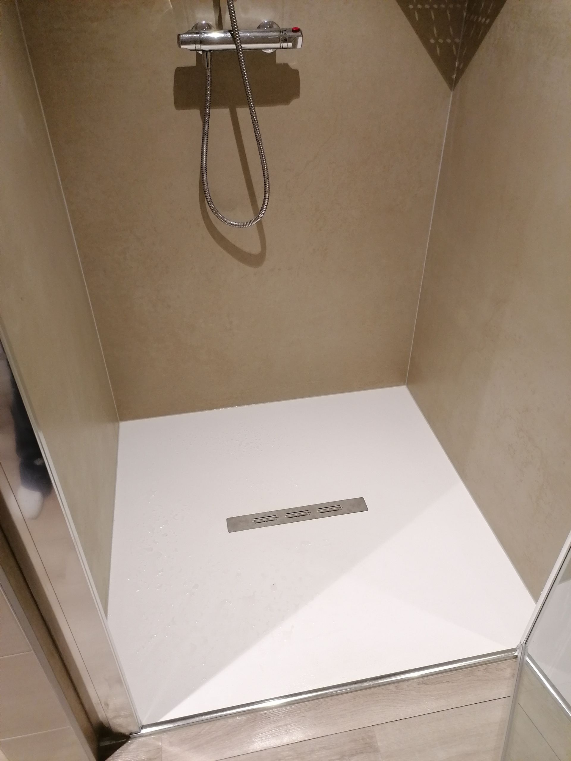 Une douche à l'italienne moderne avec des murs beiges, un sol blanc, une bonde linéaire centrale et une robinetterie de tête chromée.