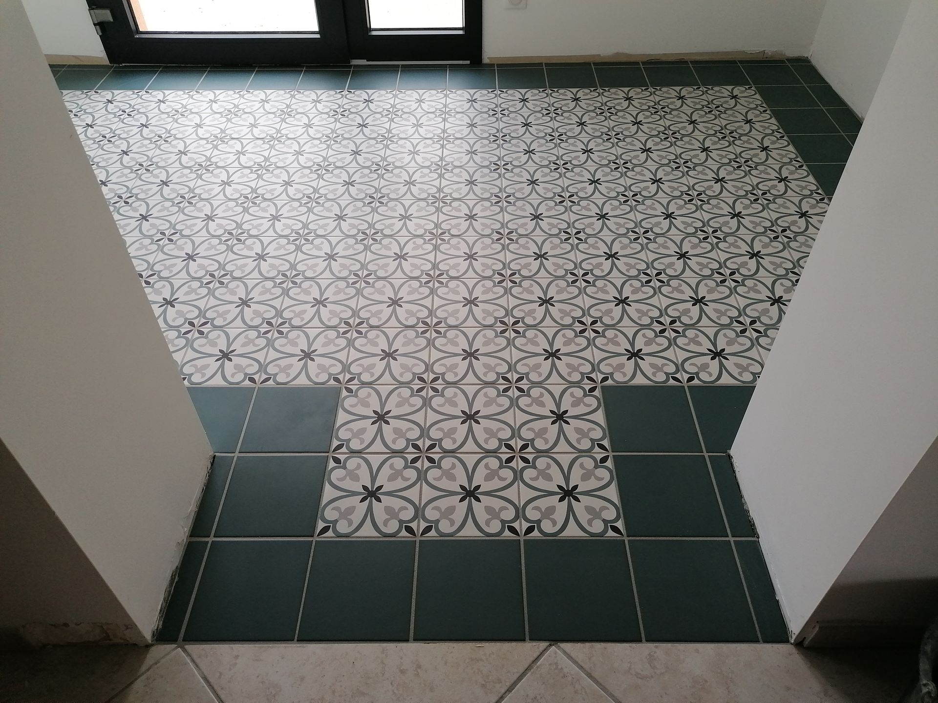 Un sol avec une partie centrale rectangulaire de carreaux blancs et noirs à motifs, bordée de carreaux unis vert foncé.