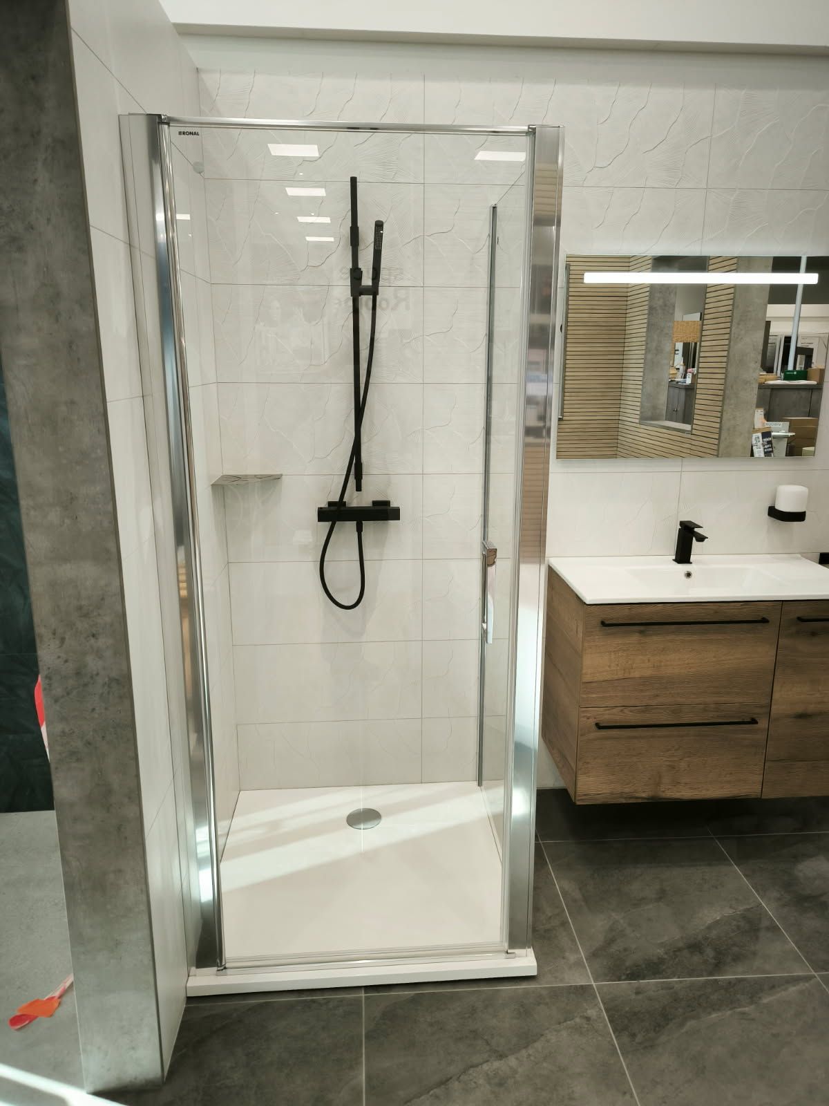 Une salle de bains moderne aménagée avec une cabine de douche en verre et une robinetterie noire, à côté d'un meuble-lavabo et d'un lavabo en bois.