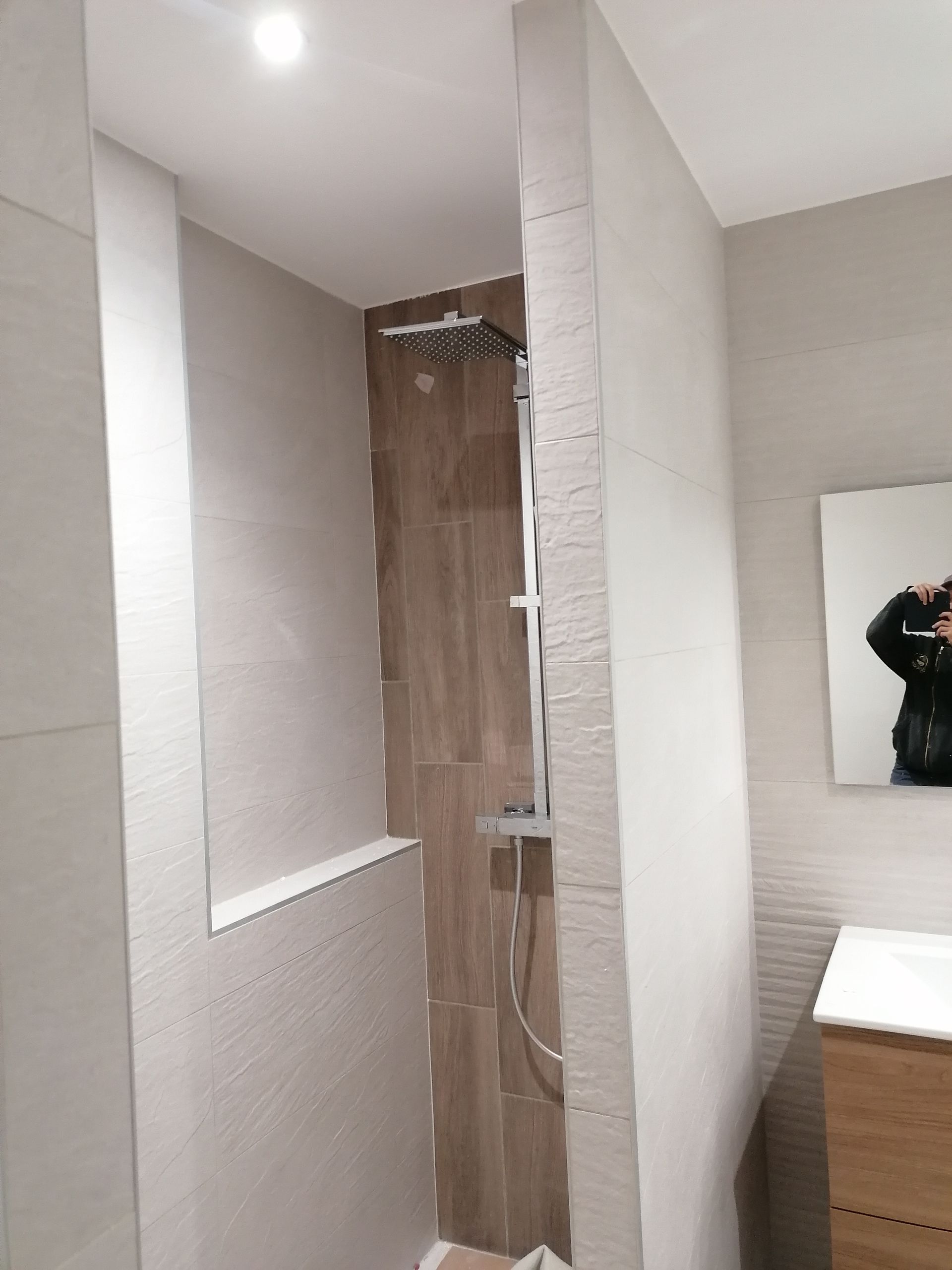 L'espace douche à l'italienne est doté de murs carrelés gris clair et d'un mur d'accent carrelé imitation bois foncé derrière les accessoires de douche.