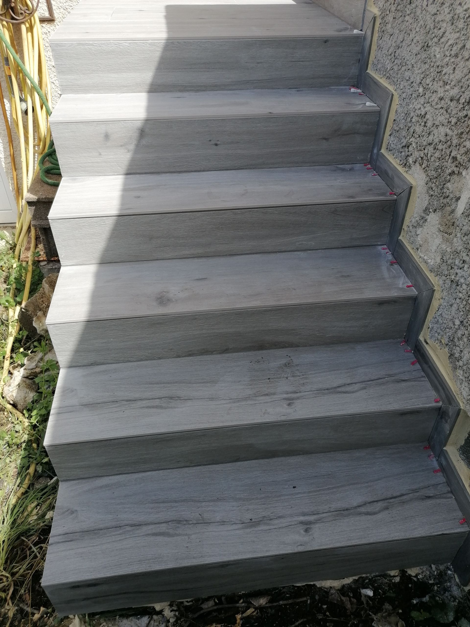 Un escalier en pierre gris clair aux bords texturés, assurant la transition entre une zone ensoleillée et un mur ombragé.