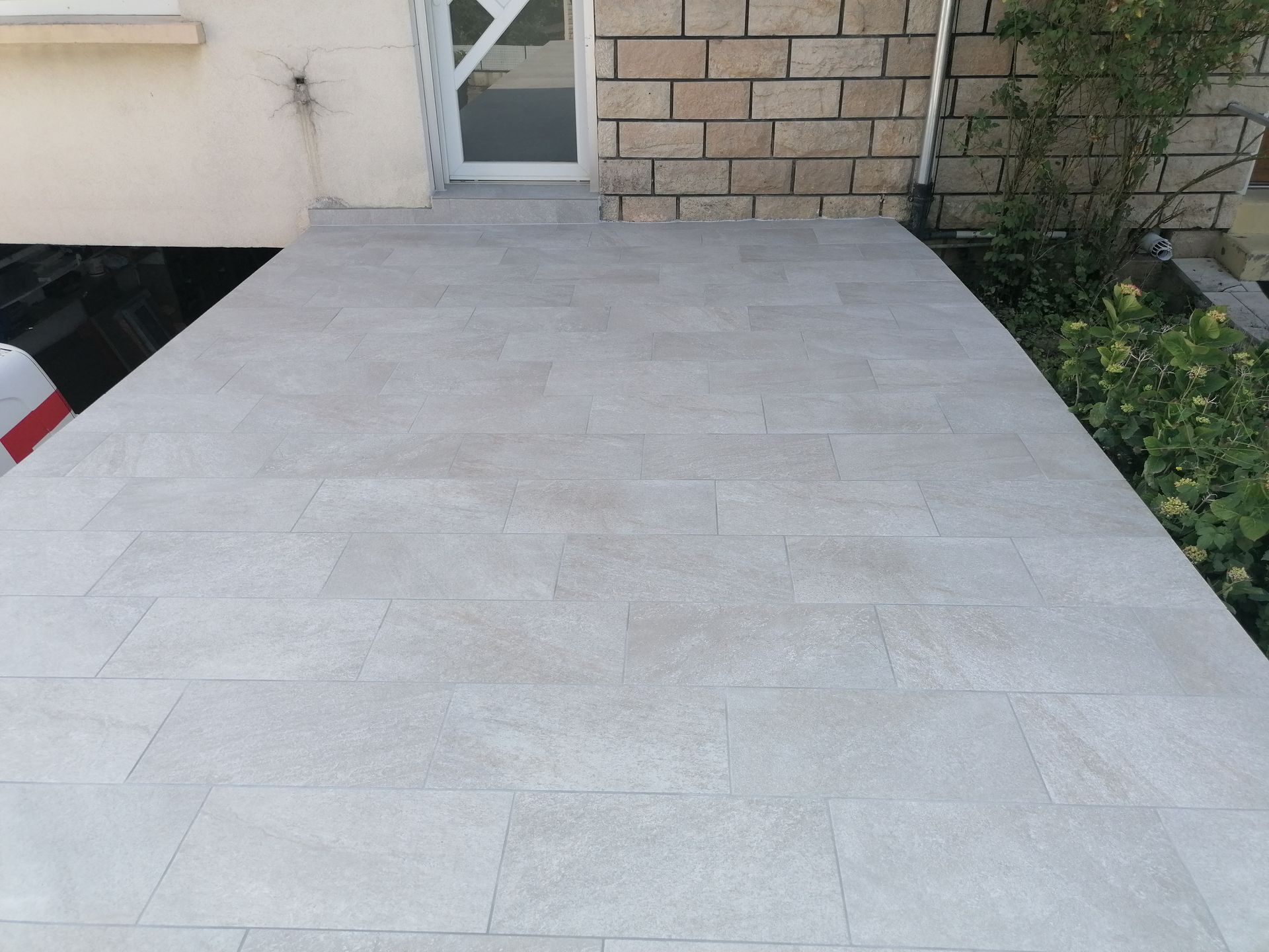 Une terrasse en pierre gris clair récemment aménagée mène à l'entrée d'une maison en briques.
