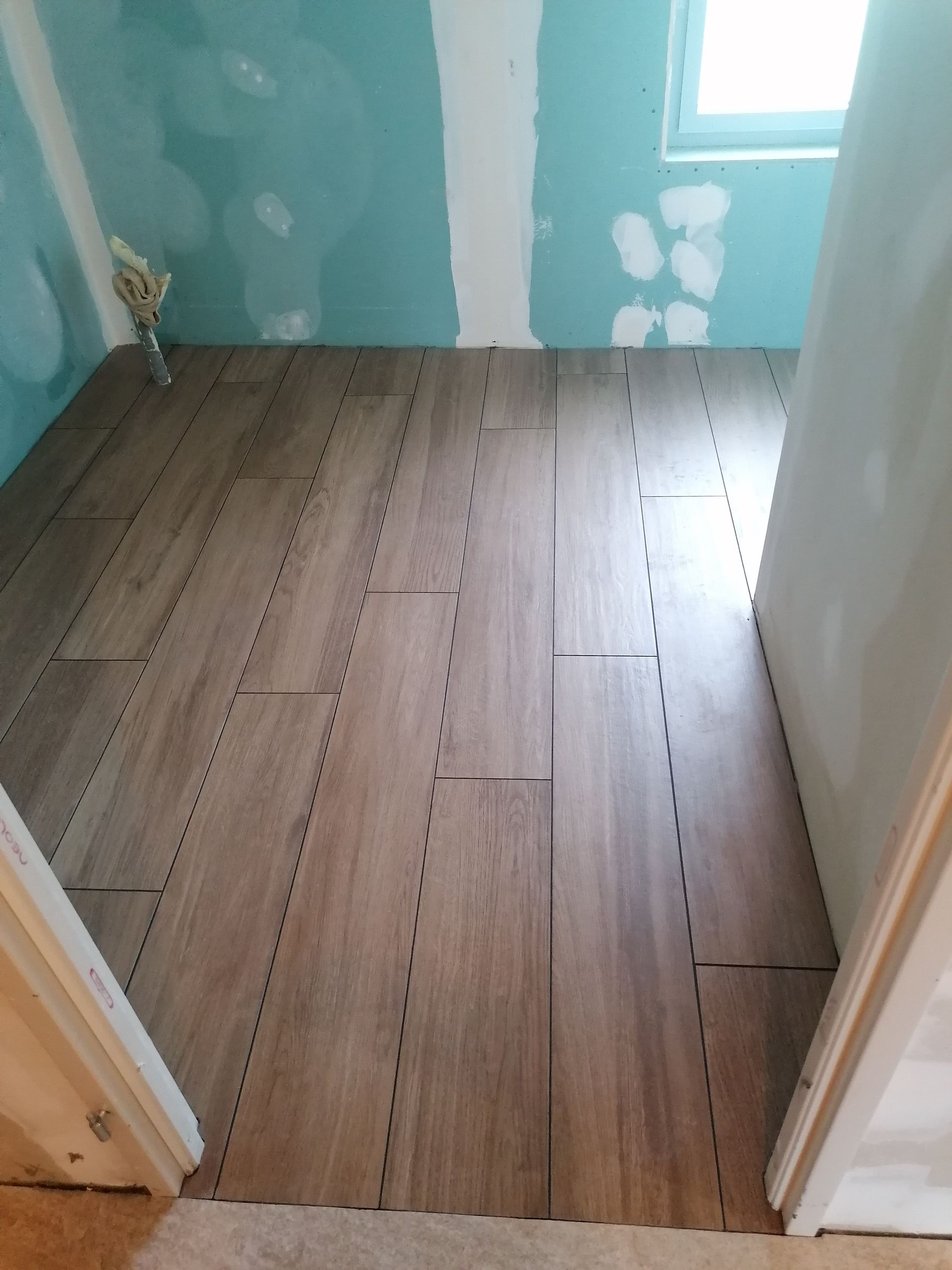 Vue à travers une porte d'une pièce aux murs en plaques de plâtre bleu clair non finies et au revêtement de sol imitation bois partiellement posé.