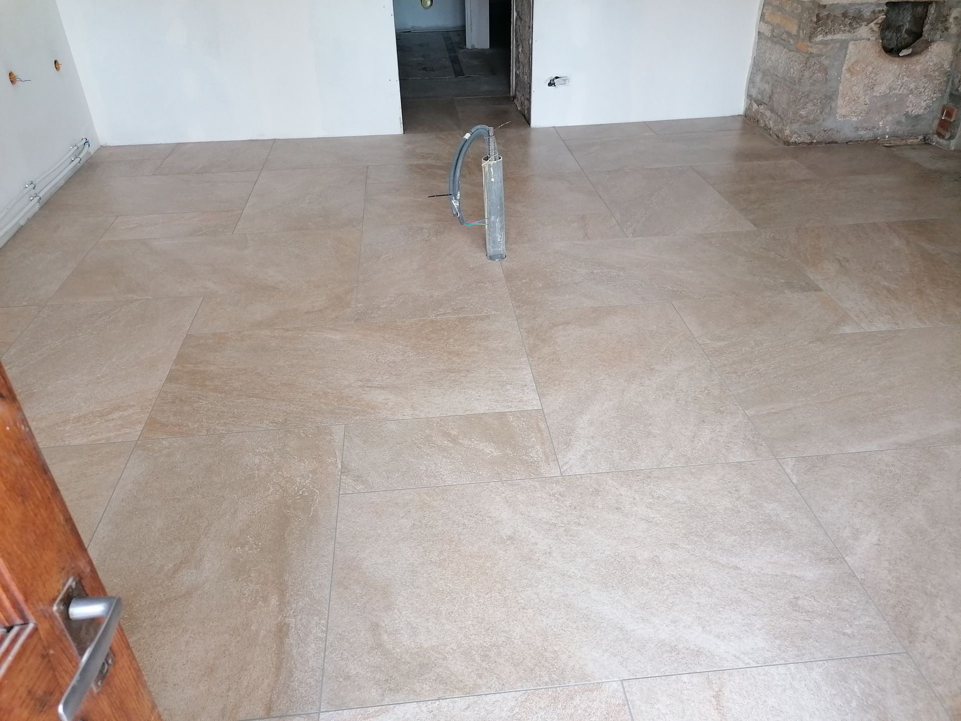 Une pièce avec des carreaux de pierre carrés aux tons neutres, posés en chevrons, et une porte inachevée au fond.