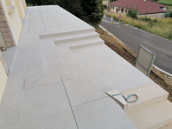 Bâtiment extérieur avec escalier en béton gris clair, situé à proximité d'une route et d'arbres verts.